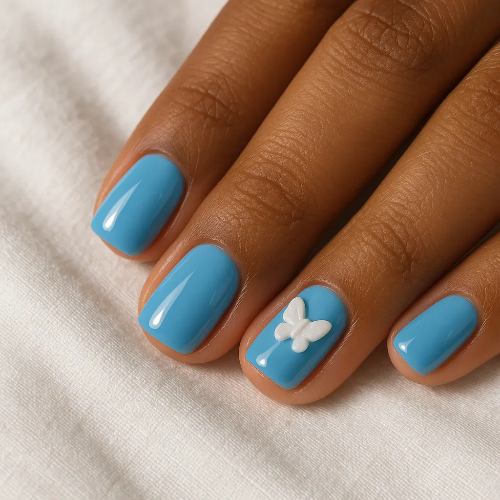 Short square nails in glossy sky blue with a small raised white butterfly on one nail, on morena skin against white linen.