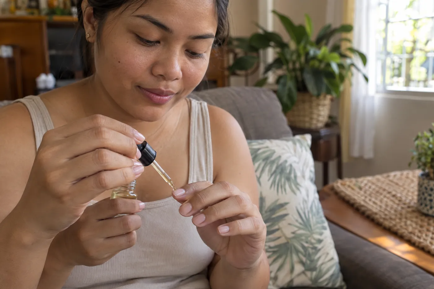 A woman on her sofa at home putting cuticle oil on her own nails with a dropper.