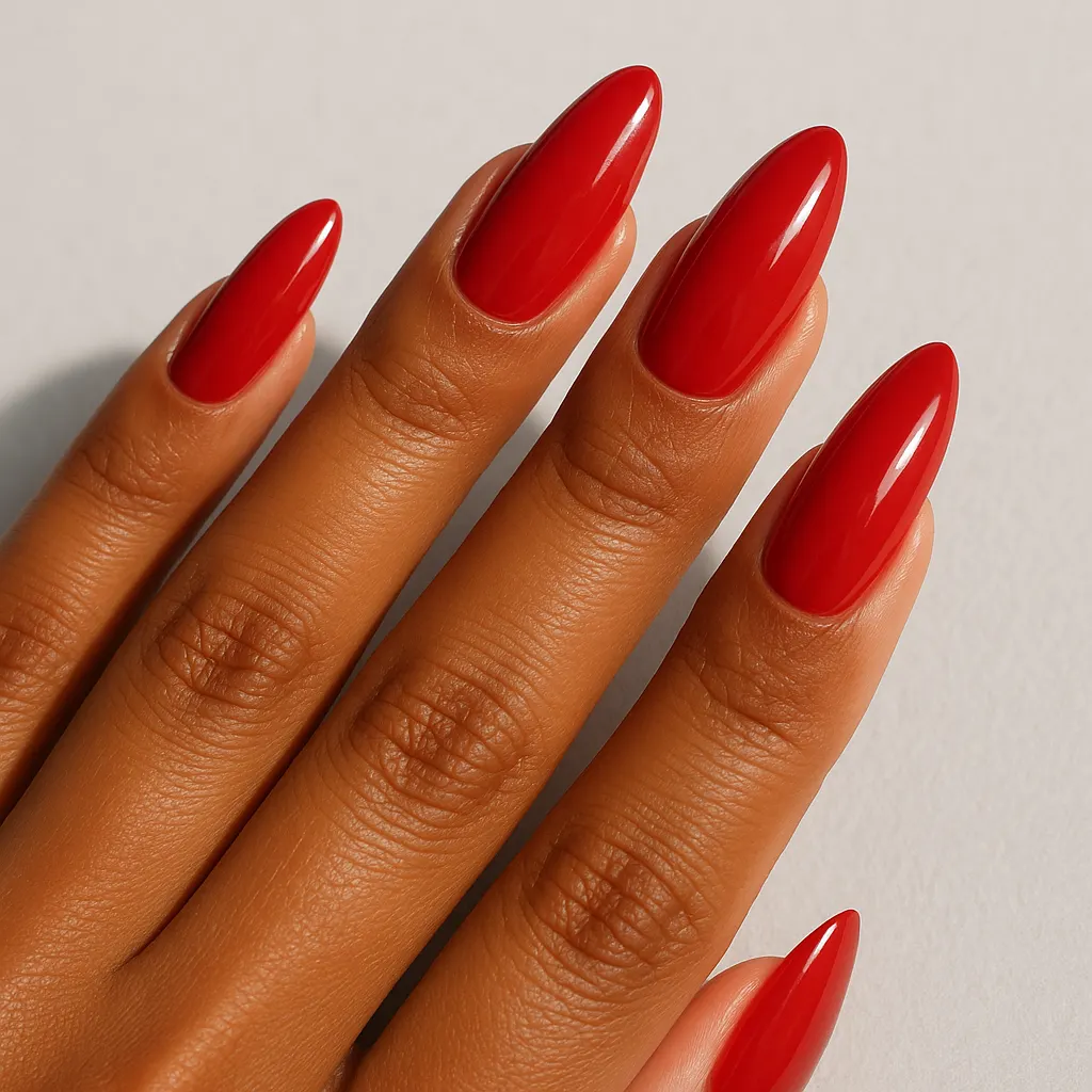 Long almond nails in a glossy true red, tapering steeply to a rounded point, on kayumanggi skin against a light grey background.