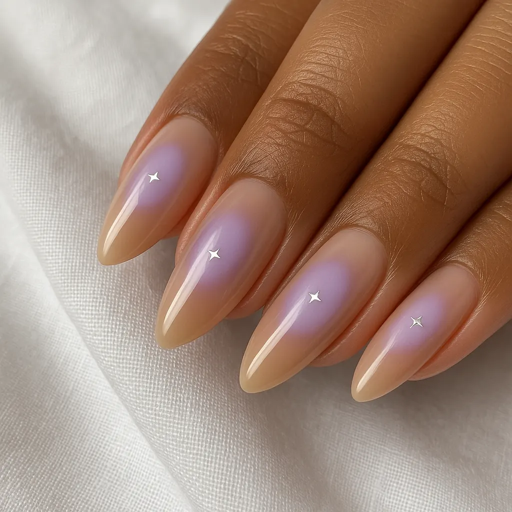 Long almond nails in sheer nude with a lilac glow and a tiny silver star in each, on warm tan skin against white linen.