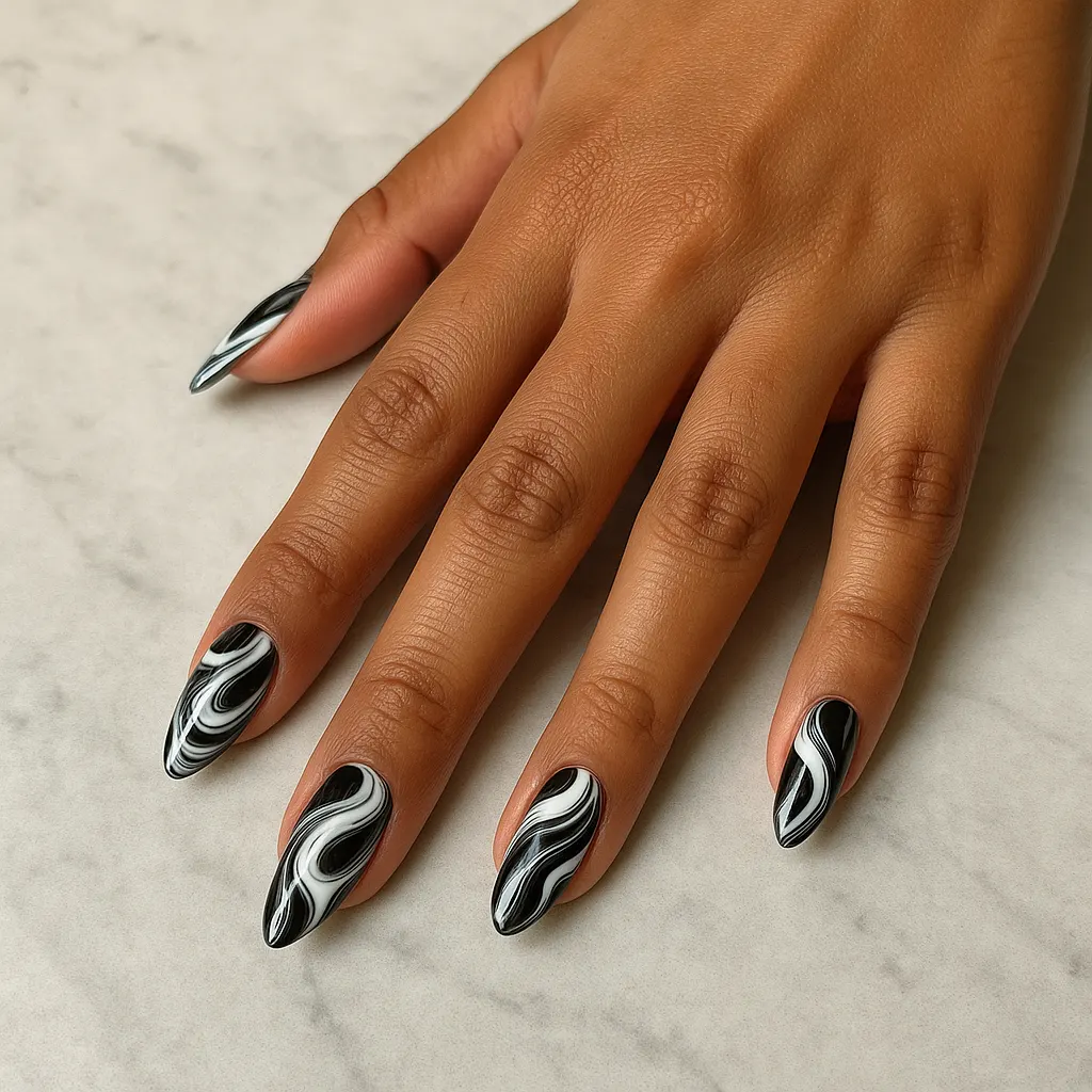 Medium almond nails with glossy black and white swirl art, on warm tan skin over grey marble.