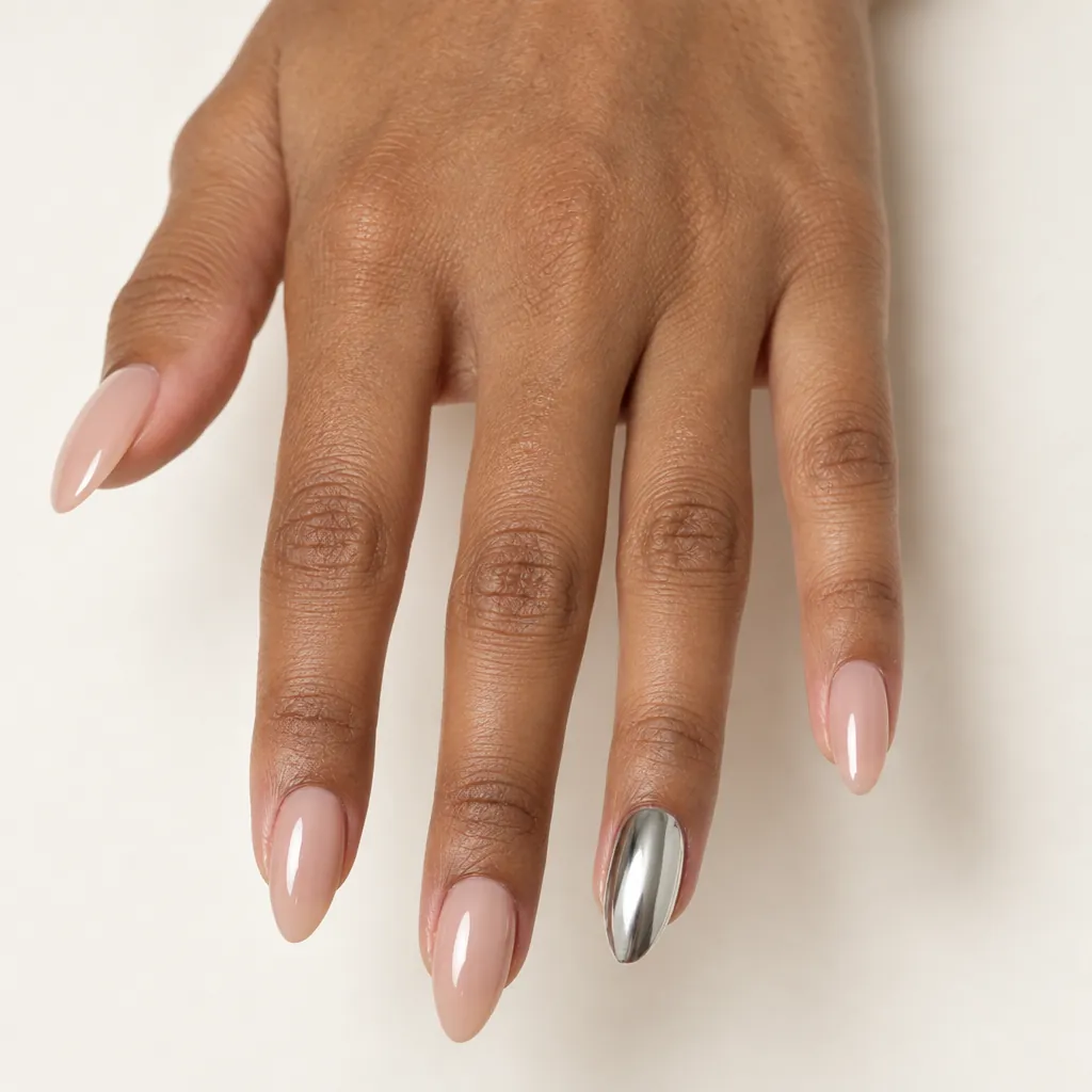 Medium almond nails in a bare nude with one silver chrome accent nail, on warm brown skin.