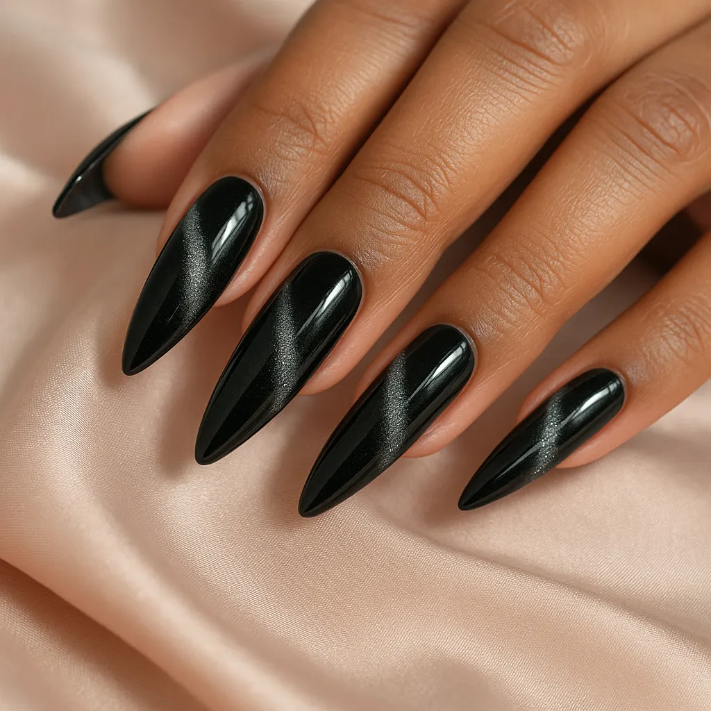 Long stiletto nail extensions in glossy black cat eye gel with a diagonal silver shimmer band, on morena skin over blush satin.