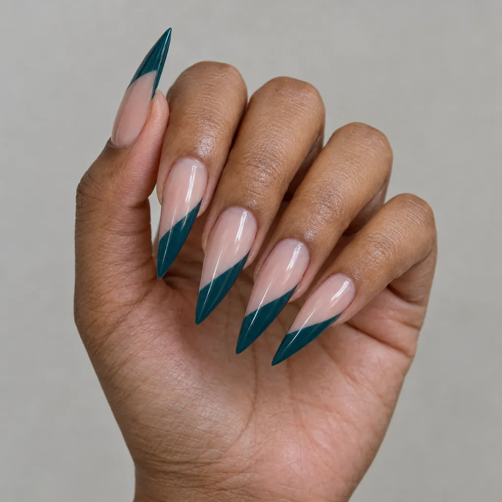 Long stiletto nails, a nude base with a deep teal tip cut on the diagonal, on medium brown skin.