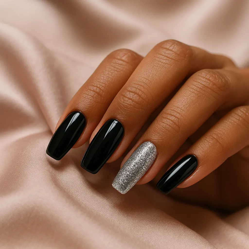 Medium coffin natural nails in glossy black gel, the ring finger in dense silver glitter, on warm tan skin, the hand on blush satin.
