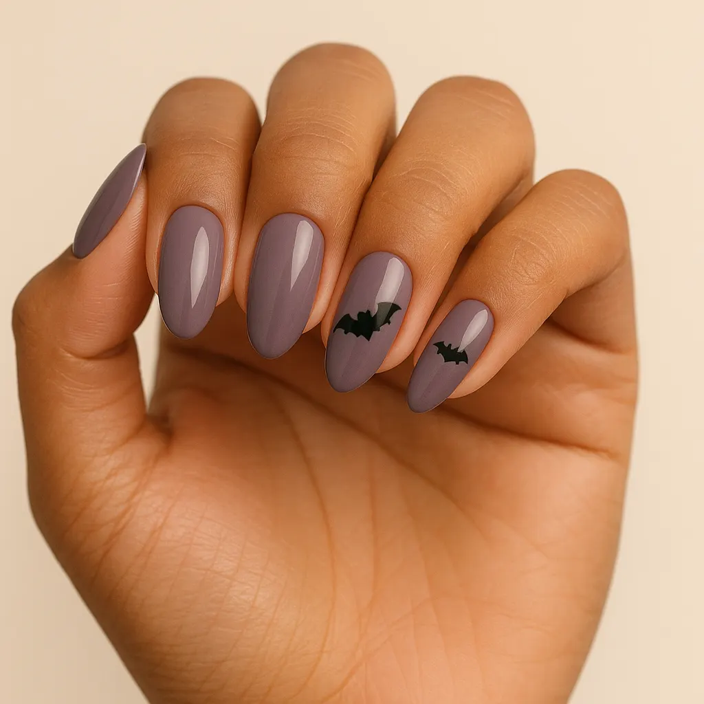Medium almond nails in a smoky mauve grey, two with small black bats, on morena skin.