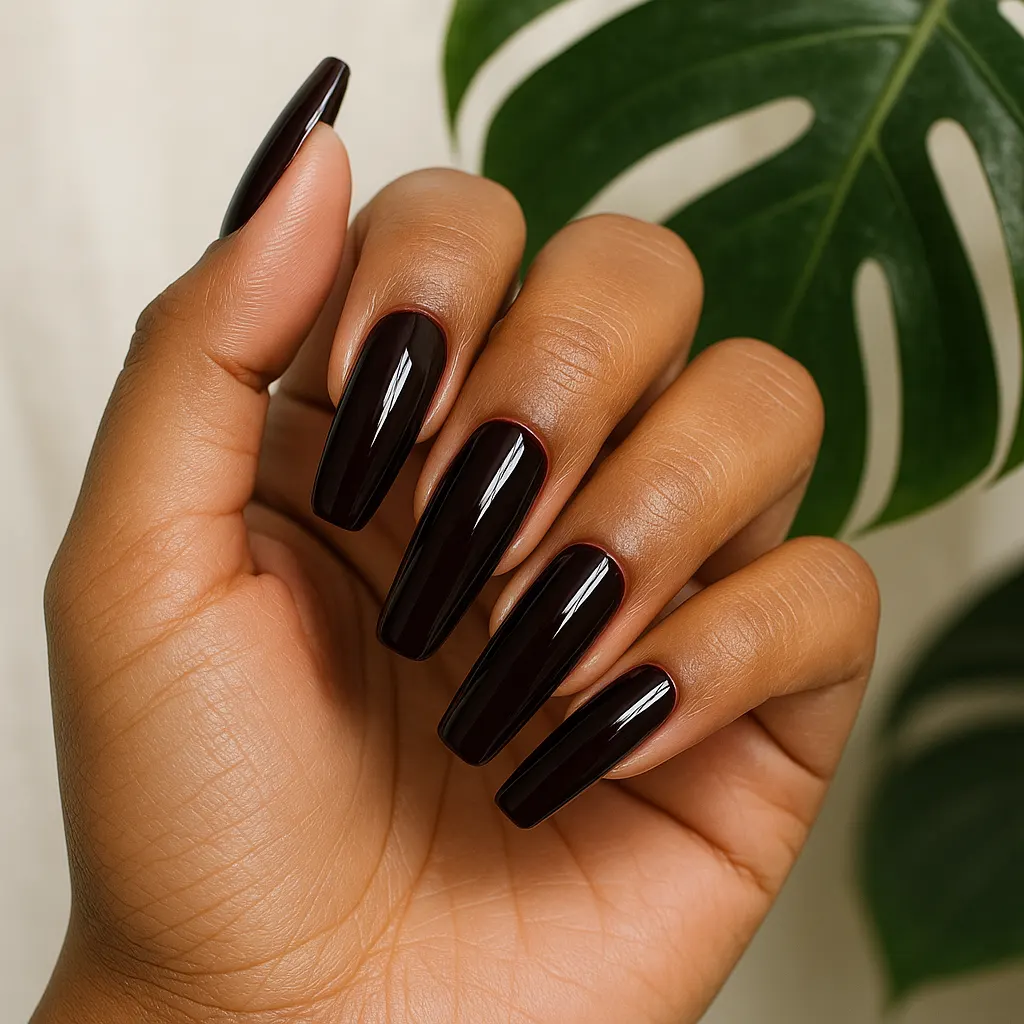 Long coffin nails in glossy oxblood, almost black-red, on warm morena skin, the hand raised in front of a monstera leaf.