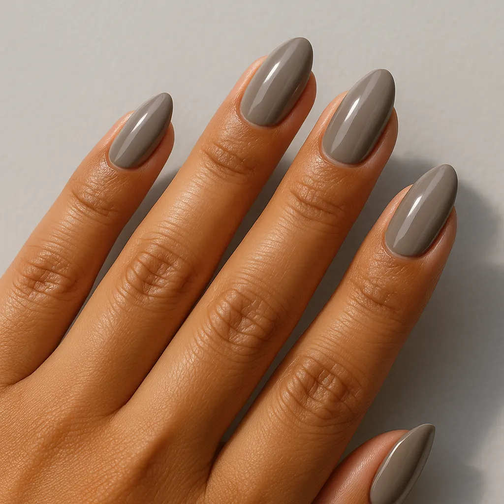 Medium almond nails in a grey-leaning greige nude on warm tan skin against a light grey background.