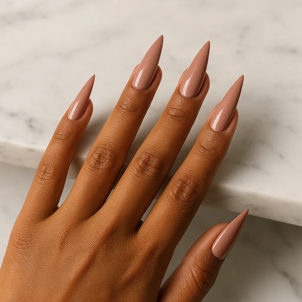 Long stiletto nails in glossy dusty rose beige nude on morena skin, resting on the edge of a white marble counter.