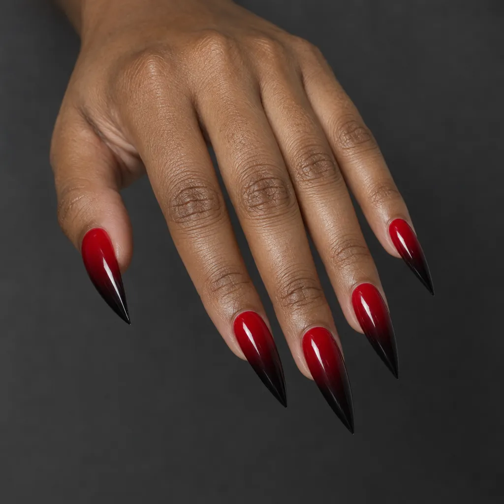 Long stiletto nails running from a bright red at the cuticle through burgundy to black at the point, on medium brown skin.