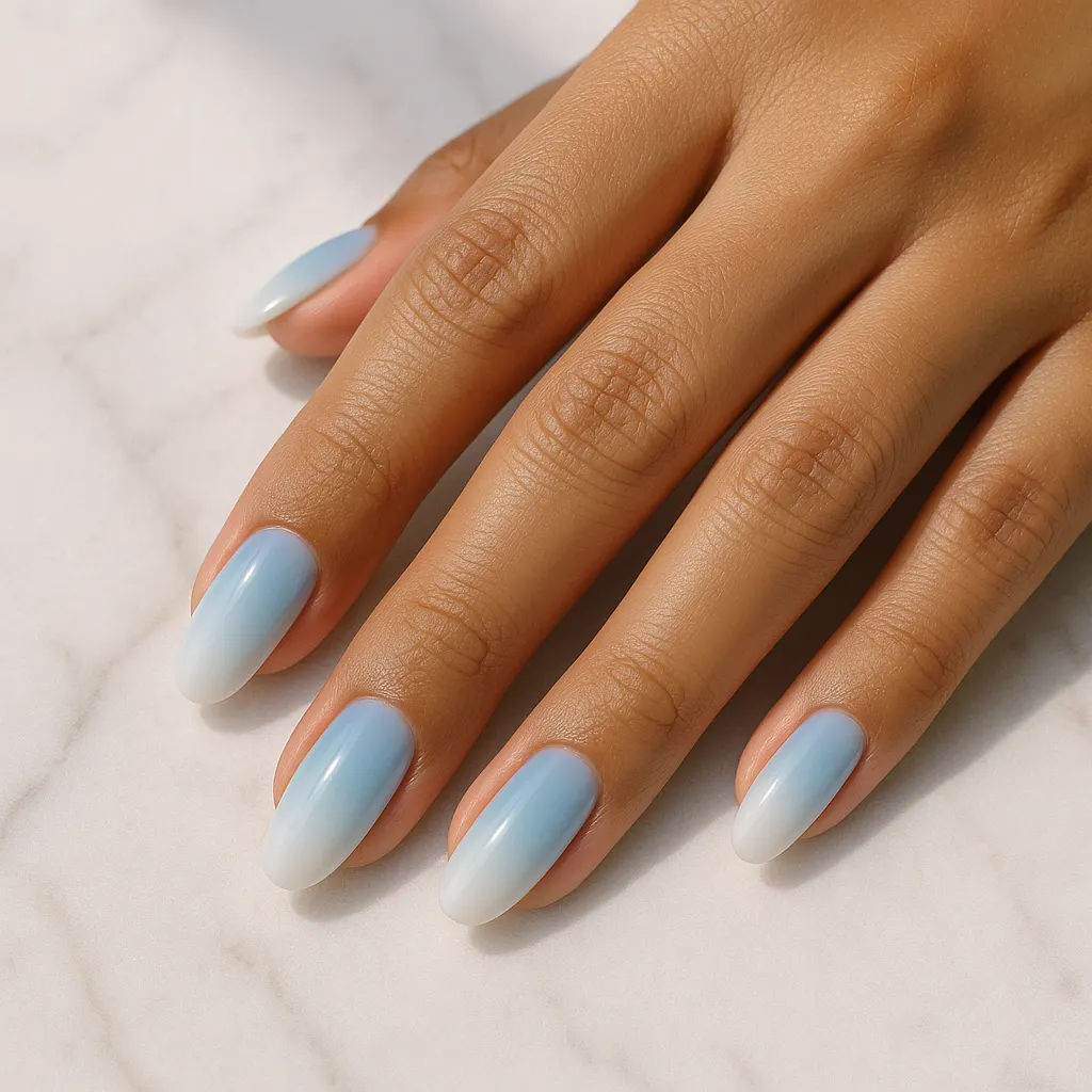 Medium oval nails fading from sky blue to milky white tips, on warm tan skin over white marble.