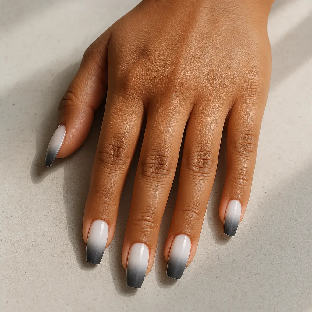 Medium coffin nails fading from bright white to charcoal grey tips, on warm tan skin resting on pale concrete.