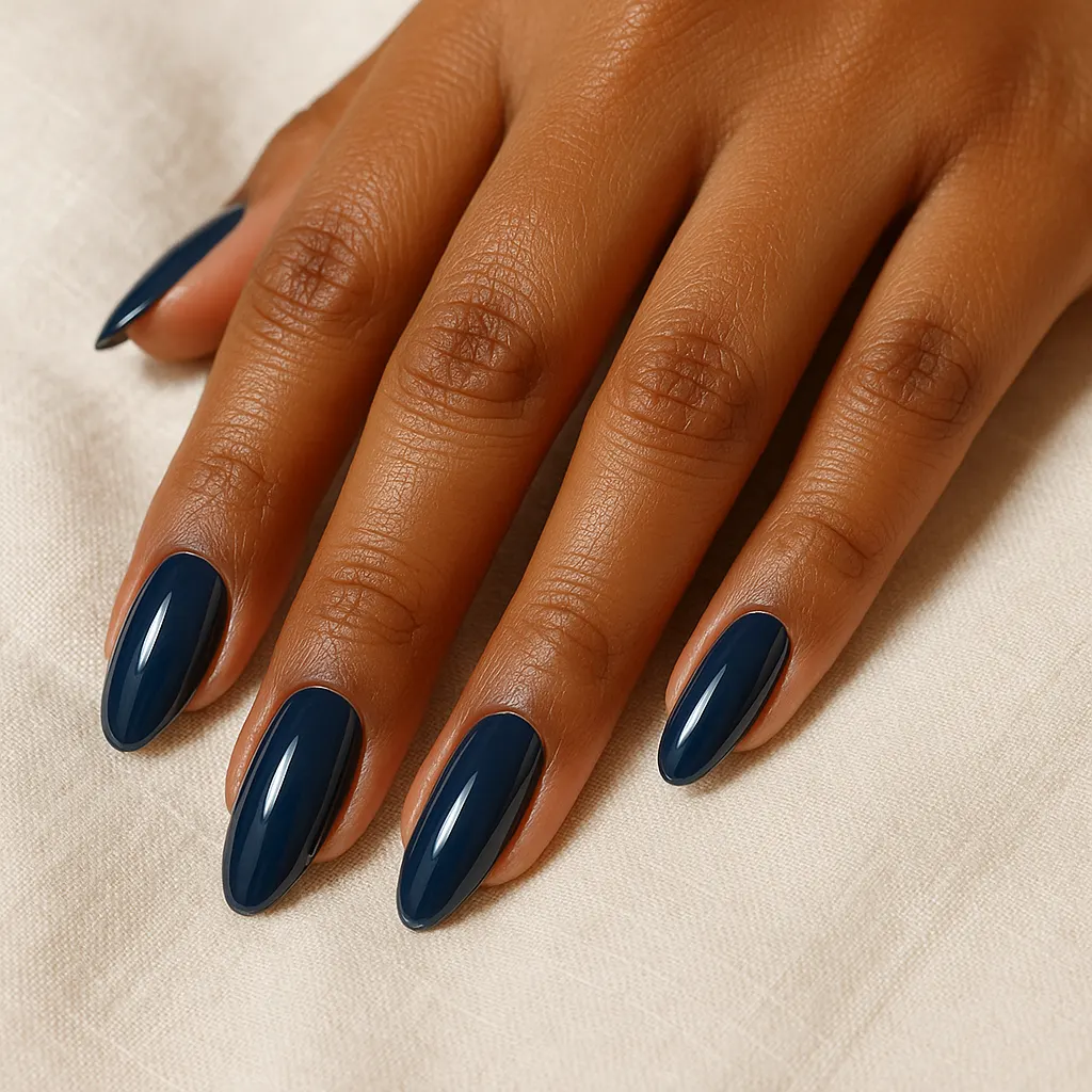Long oval nails in glossy navy blue on kayumanggi skin, the hand resting flat on cream linen.