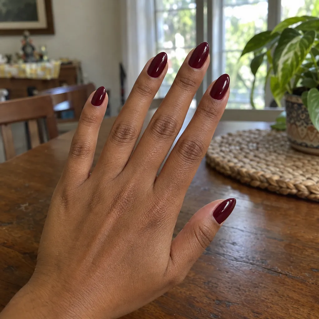 Medium almond nails in a deep oxblood wine red on brown skin.